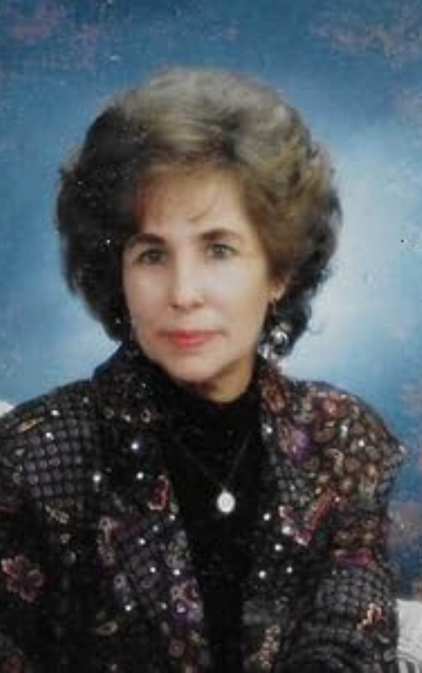 Professional author portrait of a woman with short styled hair, wearing a patterned jacket and earrings against a soft blue studio background
